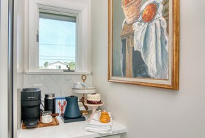 A kitchen with a coffee maker, a cake on a stand, and a painting on the wall.