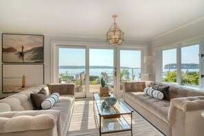 A spacious living room with two sofas, a coffee table, and a large window offering a view of the sea.