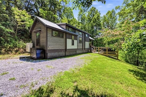 A rustic cabin with a gravel driveway, surrounded by lush greenery and trees.