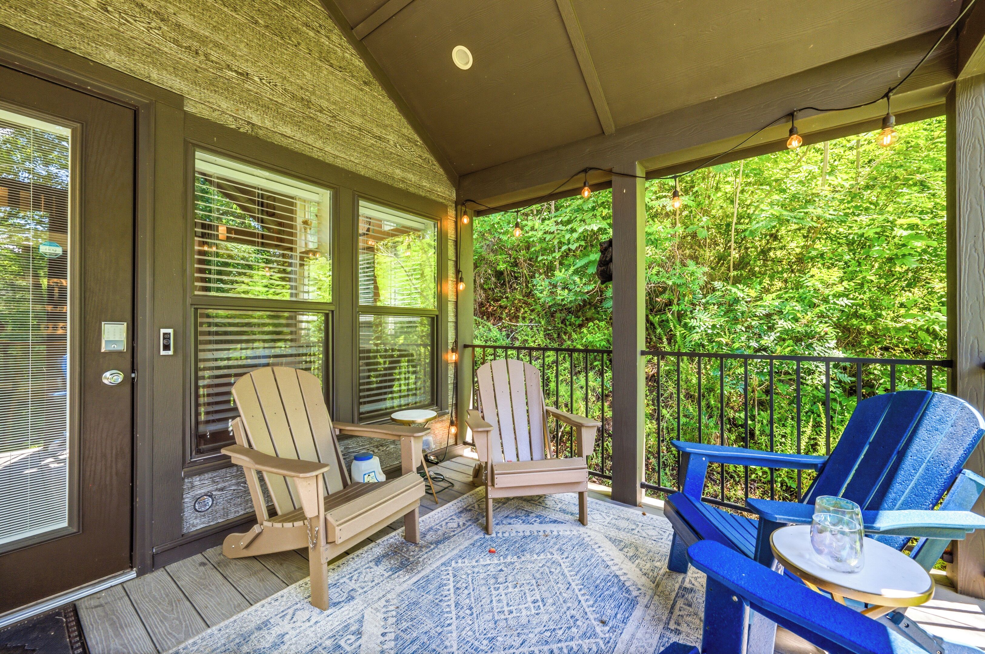 A covered porch with Adirondack chairs, a small table, and a glass of water.