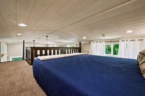 Une chambre avec un grand lit, une tête de lit en bois, un ventilateur de plafond et une vue sur la verdure.