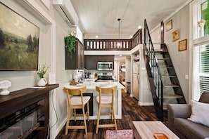A modern kitchen with a central island, wooden flooring, and a loft bedroom above.