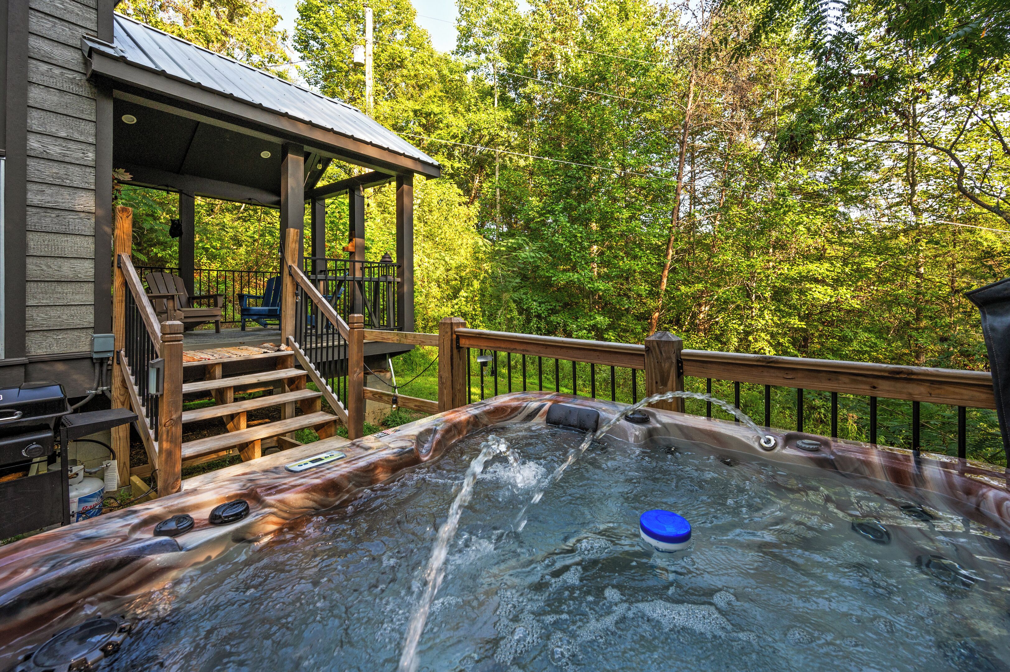Een hottub met een houten terras en een trap naar een overdekt gebied met buitenmeubels.
