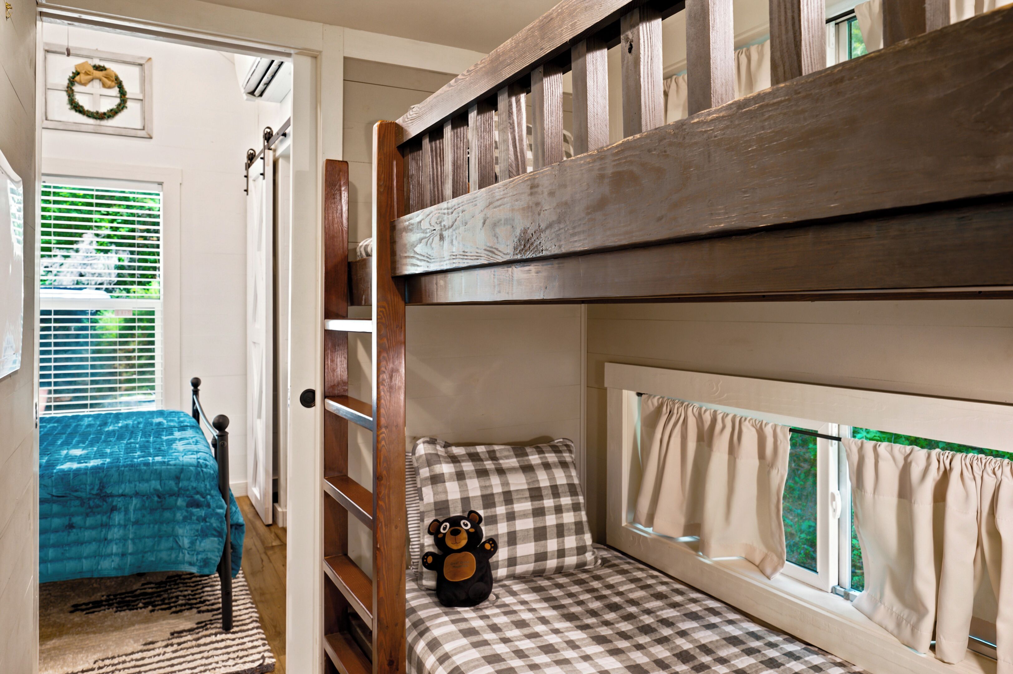 A bunk bed room with a window, a teddy bear, and a checkered bedspread.