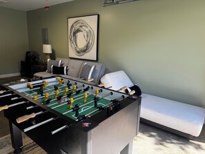 Una habitación con mesa de fútbol, sofá, lámpara y una obra de arte en la pared.