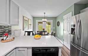 A modern kitchen with a central island, stainless steel appliances, and a dining area with a view. - Adorable 2-bedroom condo in charming Arden near airport (Arden)