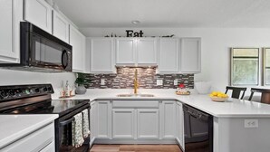 A modern kitchen with white cabinetry, a black stove, and a tiled backsplash. - Adorable 2-bedroom condo in charming Arden near airport (arden)