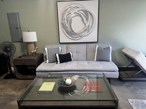 Ein Wohnzimmer mit grauem Sofa, einem Glastisch und einem an der Wand hängenden abstrakten Kunstwerk.