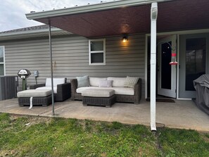 Eine überdachte Terrasse mit einer Eckcouch, Außenbeleuchtung und einem überdachten Eingangsbereich.