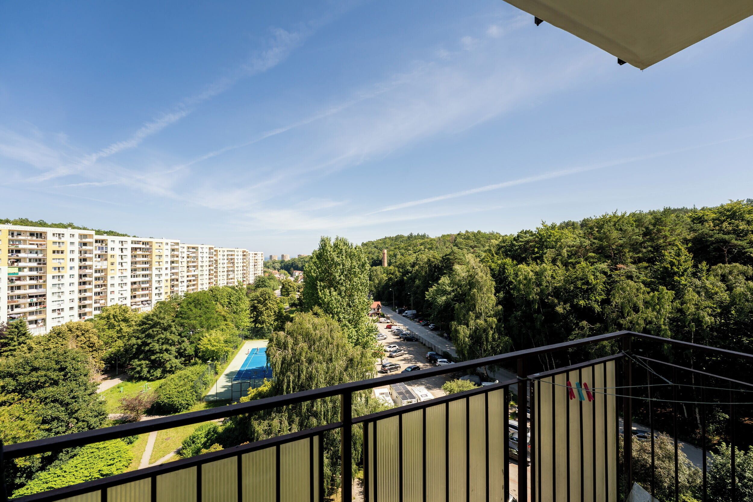 A residential area with multi-story apartment buildings, a blue-roofed sports facility, and a road with parked cars.
