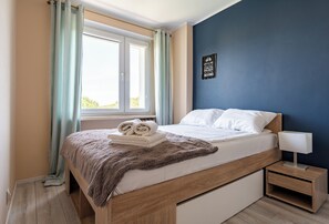 Een slaapkamer met een bed, nachtkastje, raam met gordijnen en een muur met een motiverende quote.