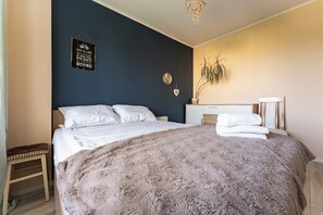 A bedroom with a bed, a bedside table, a nightstand, a wall-mounted clock, a potted plant, and a motivational quote on the wall. - Cieszyńskiego Harmony Apartment (Sopot)