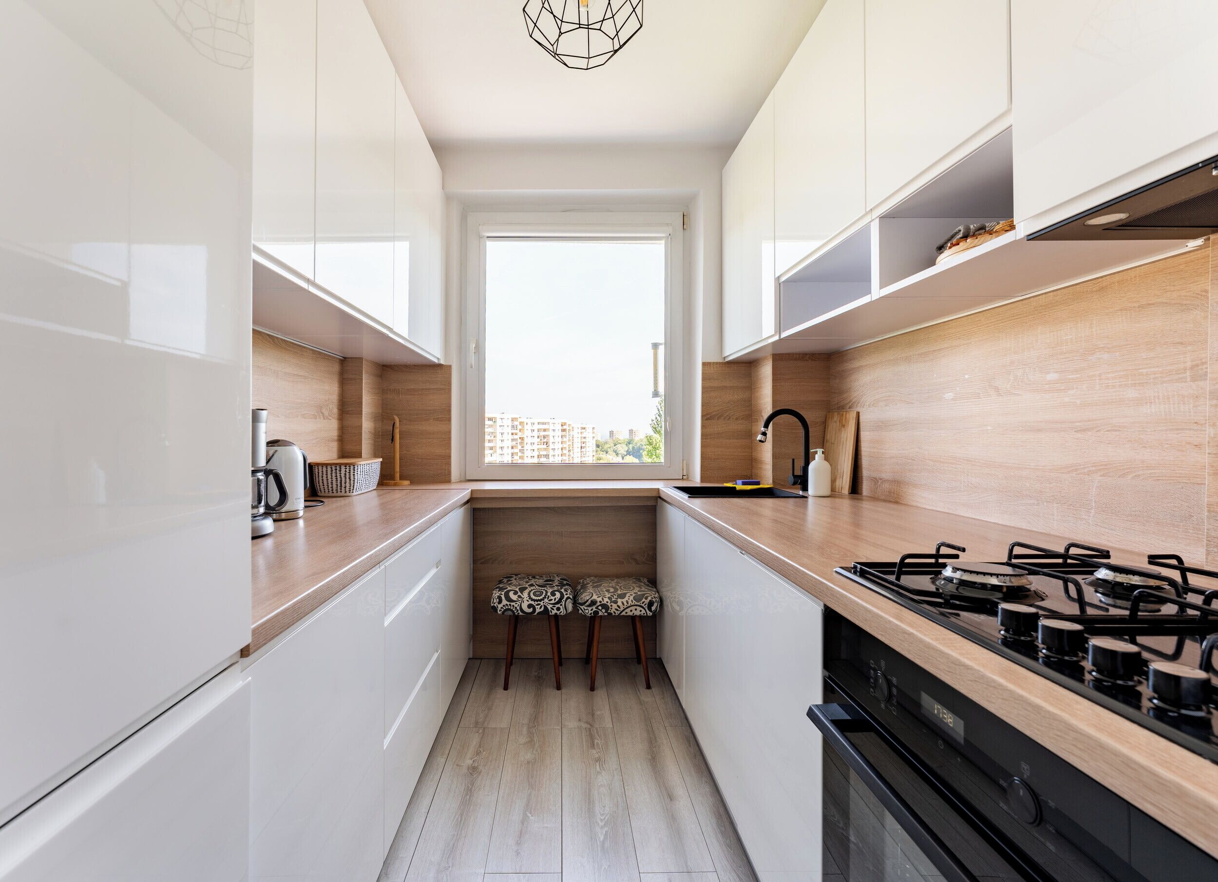 Eine moderne Küche mit weißen Schränken, einer Holz Arbeitsplatte, einem Gasherd und einem Fenster mit Blick auf Gebäude.