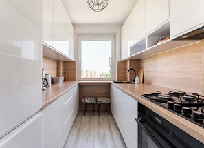 A modern kitchen with white cabinets, a wooden countertop, a gas stove, and a window providing a view of buildings outside. - Cieszyńskiego Harmony Apartment (Sopot)