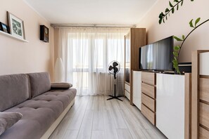 Een moderne woonkamer met een bank, een televisie, een ventilator en een plant.