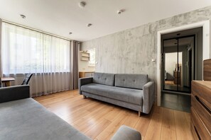 A modern living room with a grey sofa, wooden flooring, and a concrete accent wall. - Brzeźno Beachside Studio (Gdańsk)