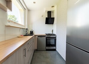 A compact kitchen with a dishwasher, stove, and a microwave above the oven. - Brzeźno Beachside Studio (Gdańsk)