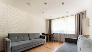 Una sala moderna con un sofá gris, una mesa de comedor con sillas y un ventanal con cortinas.