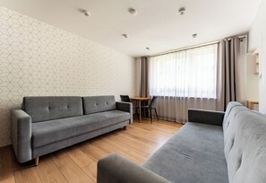 Ein modernes Wohnzimmer mit einem grauen Sofa, einem Esstisch mit Stühlen und einem Fenster mit Vorhängen.