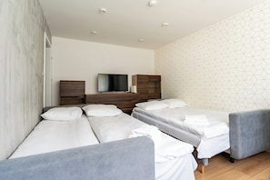 Ein Hotelzimmer mit zwei Einzelbetten, einem Fernseher, einer Holzkommode und einer Wand mit geometrischem Muster.
