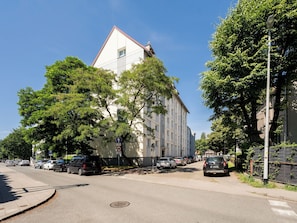 A multi-story building with a white facade and a red roof, surrounded by trees and parked cars on a clear day. - Brzeźno Beachside Studio (Gdańsk)