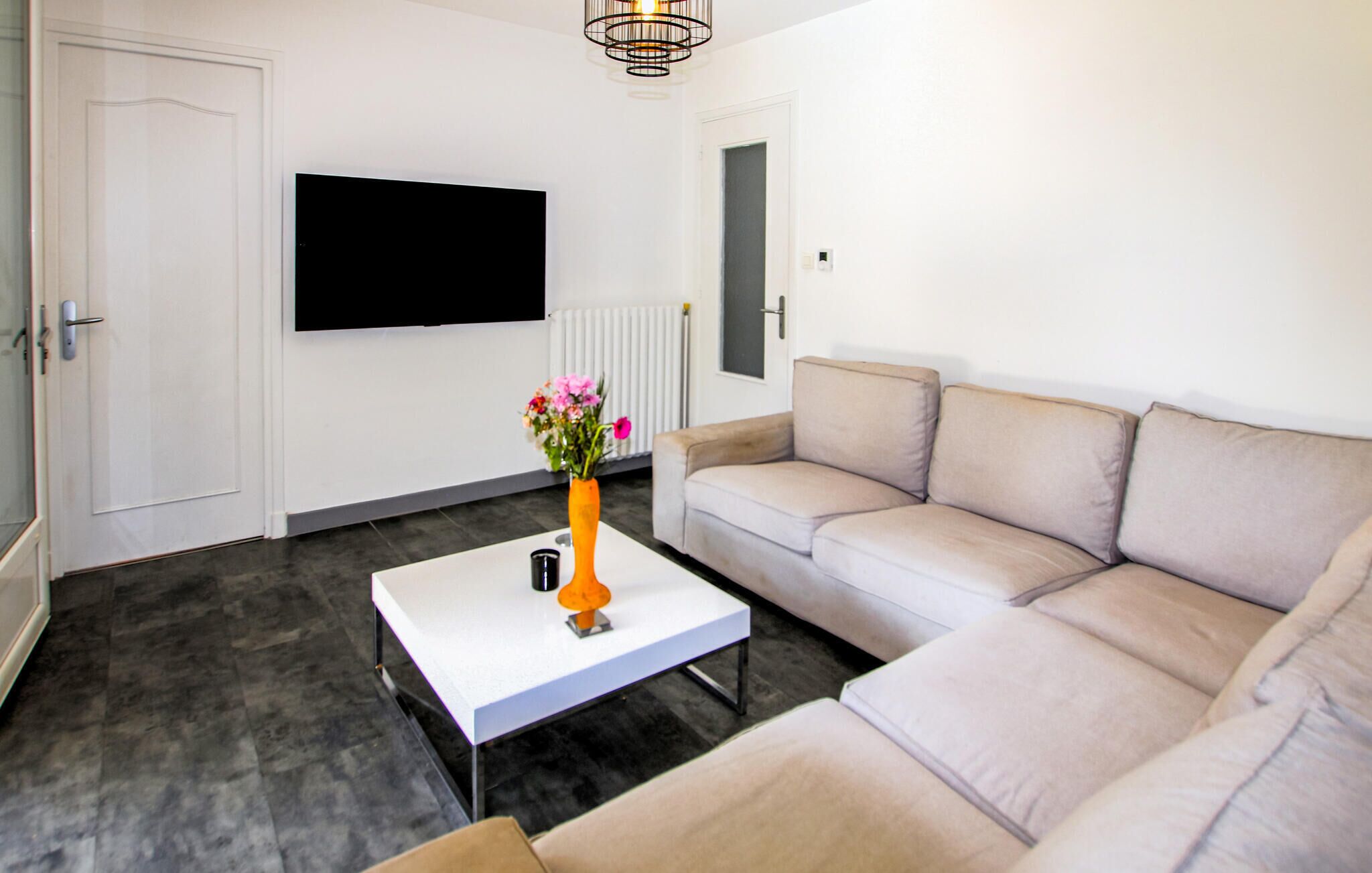 Een moderne woonkamer met een bank, een salontafel, een aan de muur bevestigde televisie en een radiator.