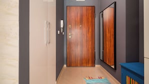 A hallway with a wooden door, a mirror, a telephone, and a colorful rug. - Ochota Superior Apartment (Warszawa)