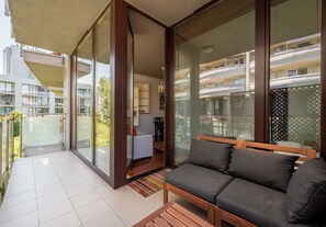 A balcony with a sofa and a dining area, glass doors leading to a room, and a view of neighboring buildings. - Ochota Superior Apartment (Warszawa)