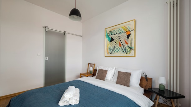 A hotel room with a bed, a painting on the wall, a radiator, and a wooden floor. - Ochota Superior Apartment (Warszawa)