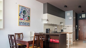 A modern kitchen with a dining area, featuring a wooden table and chairs, a kitchen island, and a colorful artwork on the wall. - Ochota Superior Apartment (Warszawa)
