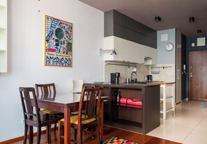 Eine moderne Küche mit Essbereich, ausgestattet mit einem Holztisch und Stühlen, einer Kochinsel und einem farbenfrohen Kunstwerk an der Wand.