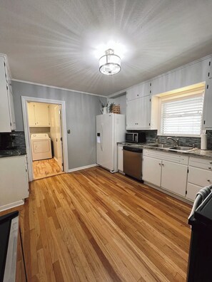 A kitchen with wooden flooring, white cabinets, a refrigerator, a dishwasher, and a microwave. - Private Cozy Room - 5 min to Hospital and Main in Fredericksburg TX 1 (Fredericksburg)
