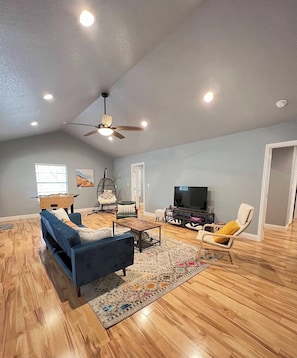 A spacious living room with a blue sofa, a wooden coffee table, a television, and a ceiling fan. - Private Cozy Room - 5 min to Hospital and Main in Fredericksburg TX 1 (Fredericksburg)