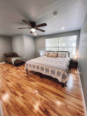 A bedroom with a wooden floor, a bed with patterned bedding, a ceiling fan, and a window with blinds. - Private Cozy Room - 5 min to Hospital and Main in Fredericksburg TX 1 (Fredericksburg)