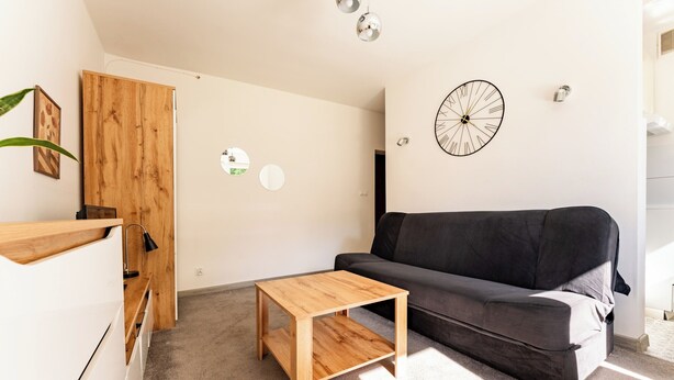 Un salon avec une table basse en bois, un canapé gris et une horloge murale.