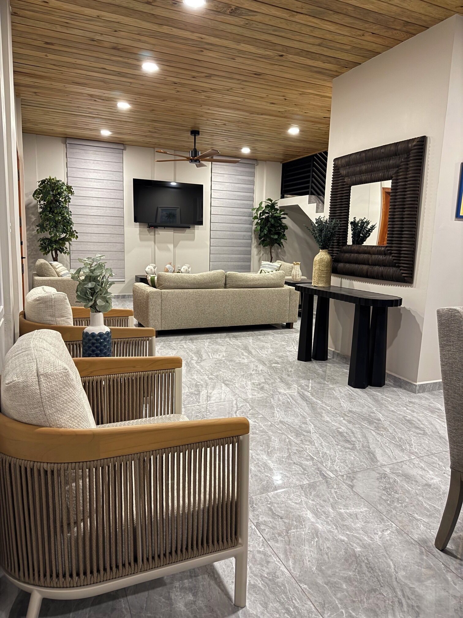 Uma sala de estar moderna com um sofá, cadeiras, uma TV e um espelho grande.