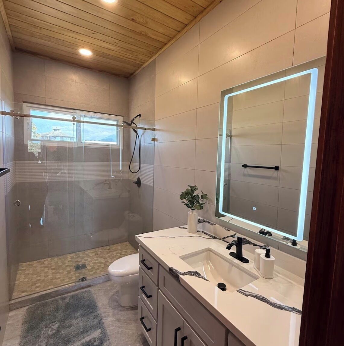 Ein modernes Badezimmer mit einer gläsernen Dusche, einem großen Spiegel und einem weißen Waschbecken.