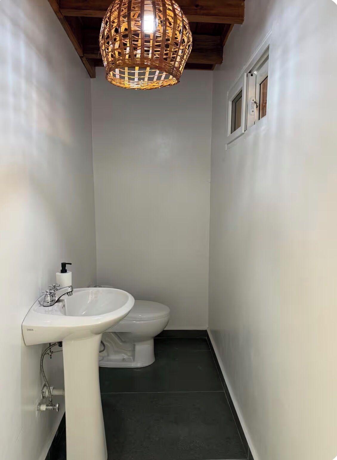 Une petite salle de bain avec un lavabo blanc, des toilettes et un luminaire suspendu au plafond en osier.