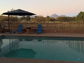 A pool area with lounge chairs and a table, surrounded by a wooden fence and desert vegetation.