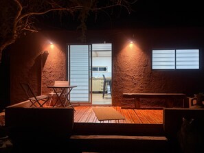 Zona d'estar a l'exterior acollidora amb un terra de fusta, una taula i cadires, que condueix a una porta corredissa de vidre que dóna a la cuina.