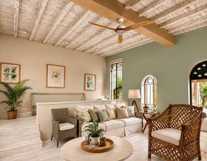 Ein Zimmer mit Deckenventilator, einer Couch, einem Korbstuhl und gerahmten Pflanzenabbildungen an der Wand.