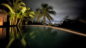 A nighttime view of a pool with palm trees and a cityscape in the background. - Luxurious & Secure Private Pool Villa in Cap Estate, St. Lucia 3 BR+3 Bathrooms (Gros Islet)