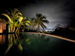 Ein Blick auf ein Pool-Gelände bei Nacht mit Palmen und einer Stadtlandschaft im Hintergrund.