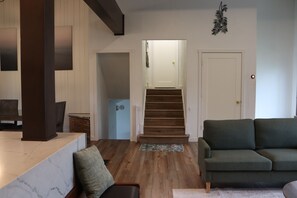 Een moderne woonkamer met een houten trap, een groene bank en een marmeren aanrechtblad.