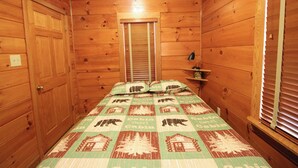 Ein Zimmer einer Holzhütte mit einem Bett, einem Nachttisch und einem Fenster mit Jalousien.