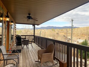 Eine Holzterrasse mit Gartenmöbeln, einem Deckenventilator und Blick auf Berge und Stromleitungen.