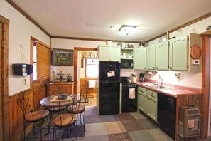 A compact kitchen with a dining area, a refrigerator, a stove, and light green cabinets. - Creekside Treehouse- Creekside Cabin (Bryson City)