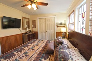 A bedroom with a bed, a ceiling fan, a TV, a dresser, a door, and a window with blinds. - Creekside Treehouse- Creekside Cabin (Bryson City)