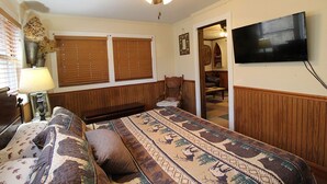 A bedroom with a bed, a ceiling fan, a television, and a window with blinds. - Creekside Treehouse- Creekside Cabin (Bryson City)