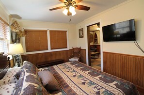 Ein Schlafzimmer mit einem Bett, einem Deckenventilator, einem Fernseher und einem Fenster mit Jalousien.